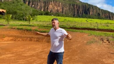 Homem em pé sobre solo vermelho em fazenda em Minas Gerais com paredão de pedra e vegetação ao fundo, em área de construção sustentável