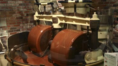 Interior de uma fábrica mostrando como o chocolate é feito na indústria, com uma máquina de conchagem em operação para refinar a textura.