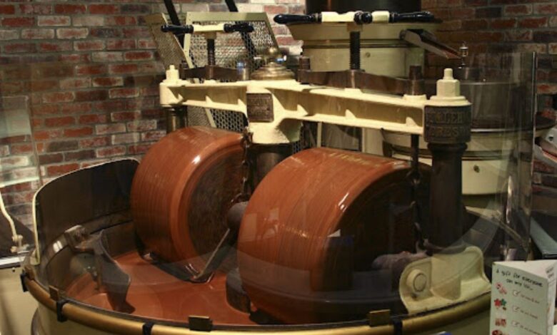 Interior de uma fábrica mostrando como o chocolate é feito na indústria, com uma máquina de conchagem em operação para refinar a textura.