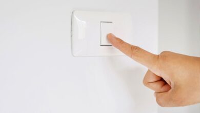 Mão de uma pessoa pressionando um interruptor de luz branco em uma parede branca.