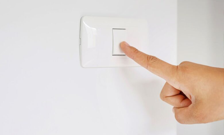 Mão de uma pessoa pressionando um interruptor de luz branco em uma parede branca.