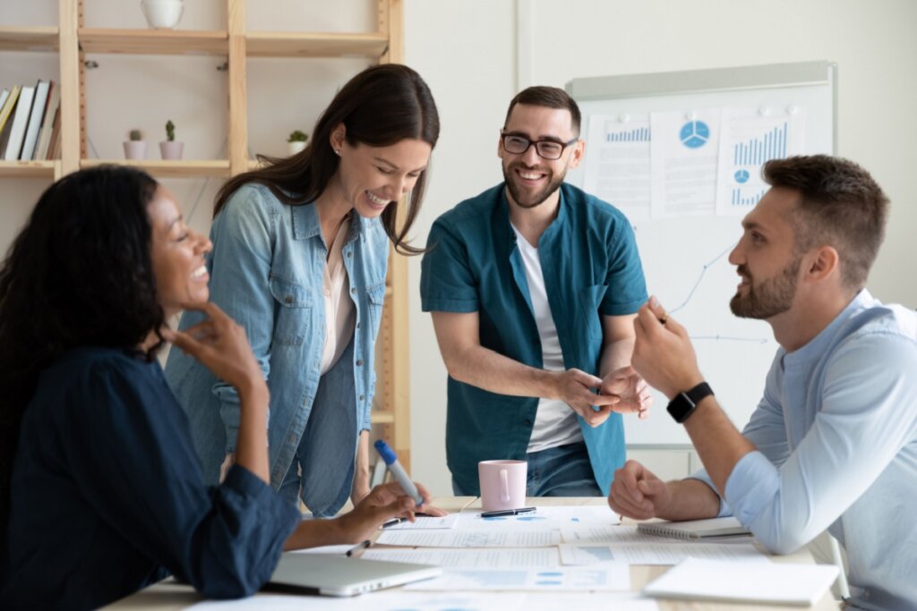 dois homens e duas mulheres sorrindo em volta de mesa em ambiente de trabalho. na mesa há diversos papéis.